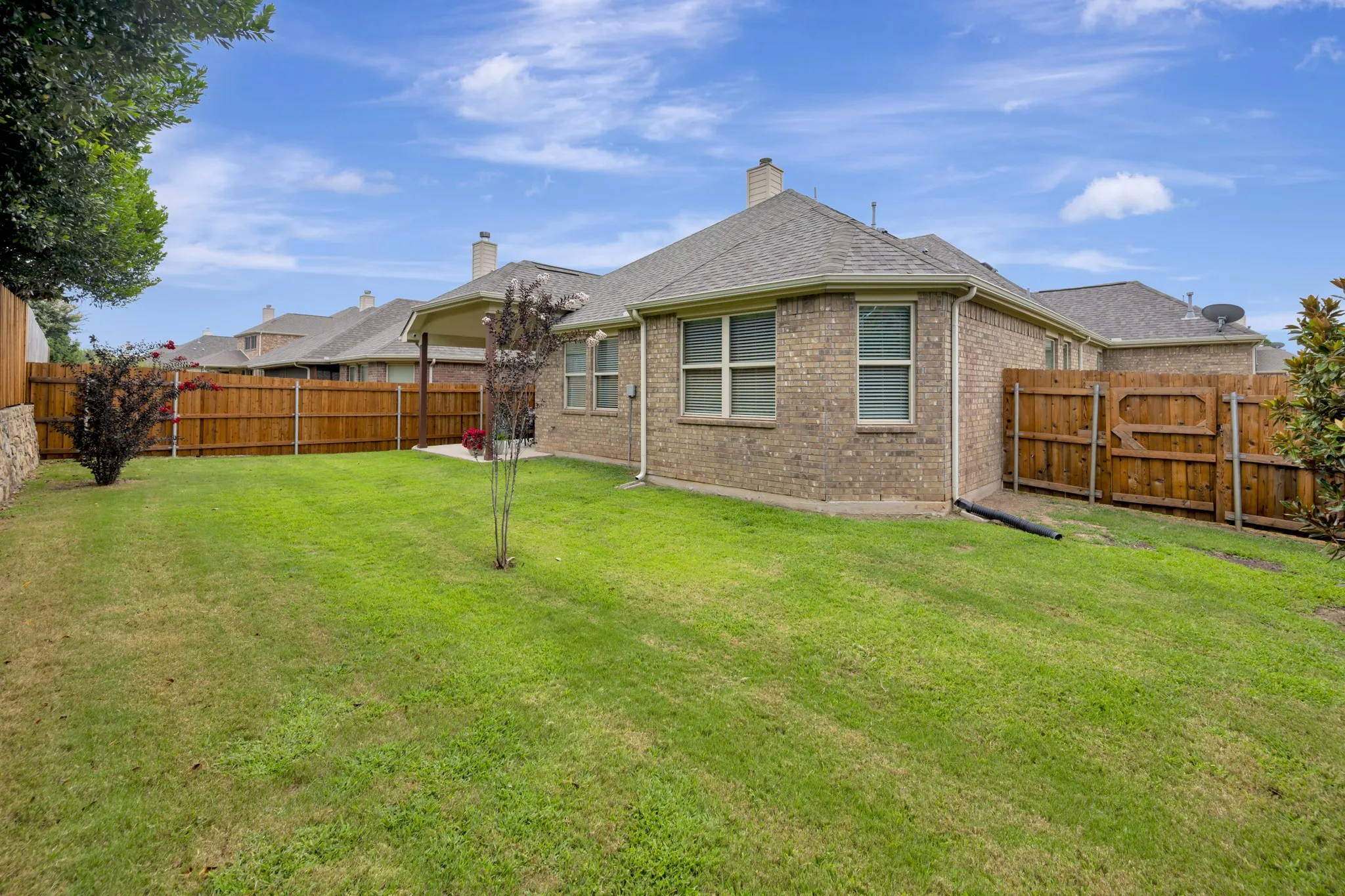Expansive fenced backyard featuring a brick exterior, covered patio, mature landscaping, and a wood privacy fence