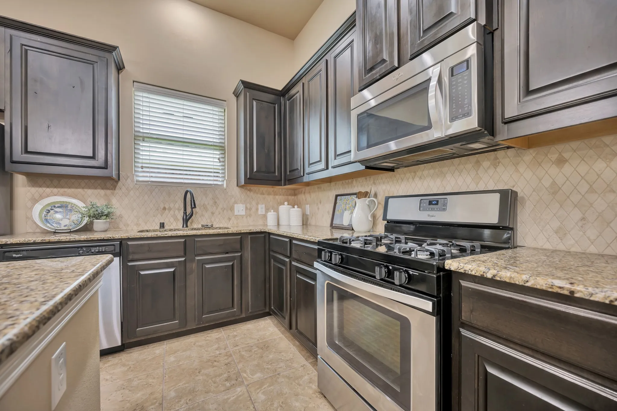 Kitchen featuring dark wood-finish cabinetry, light-toned granite countertops, and a diagonal tile backsplash
