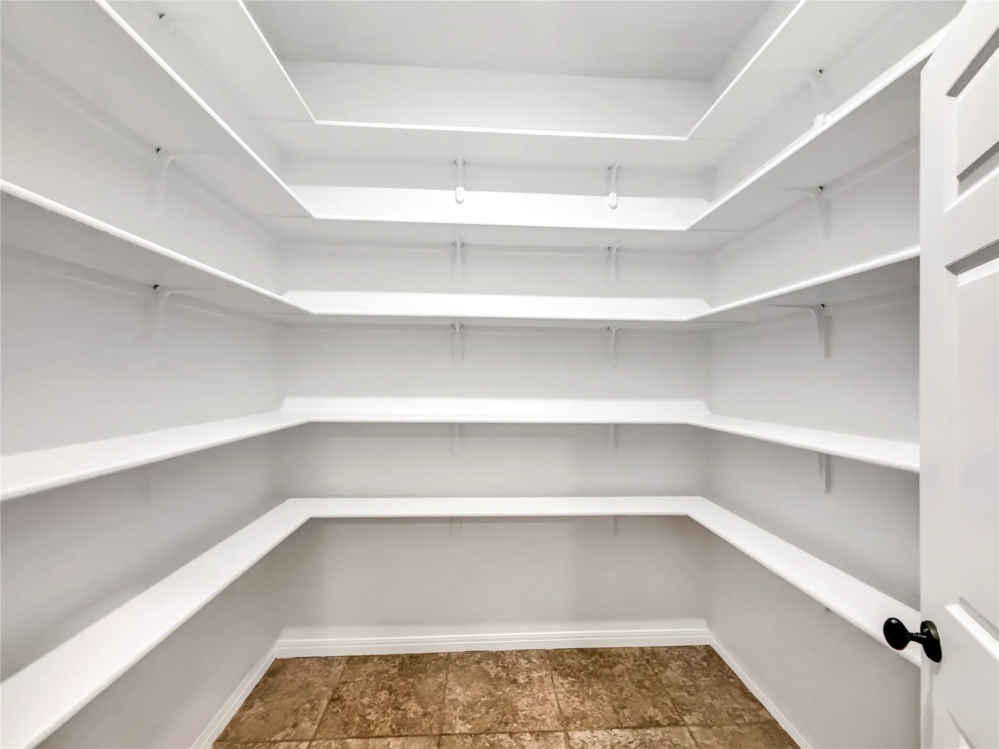 Walk-in pantry featuring expansive white shelving, integrated architectural lighting, and neutral-toned floor tile