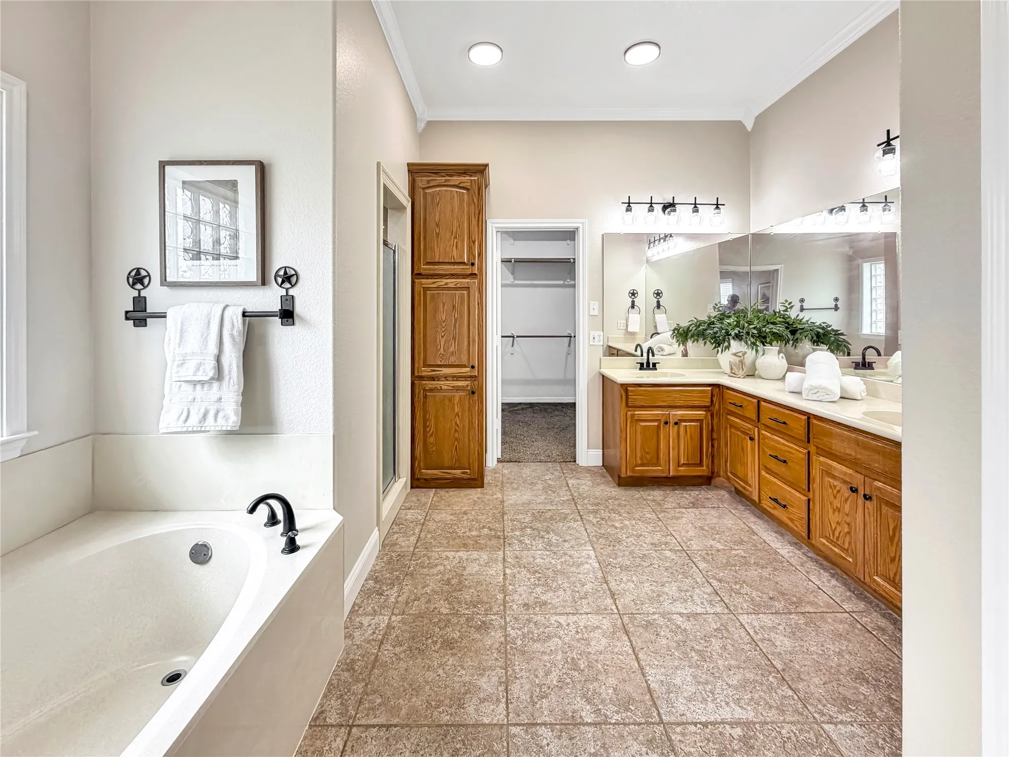 Spacious bathroom featuring an integrated soaking tub, dual vanity with wood cabinetry, a built-in storage cabinet, and large-format floor tiling