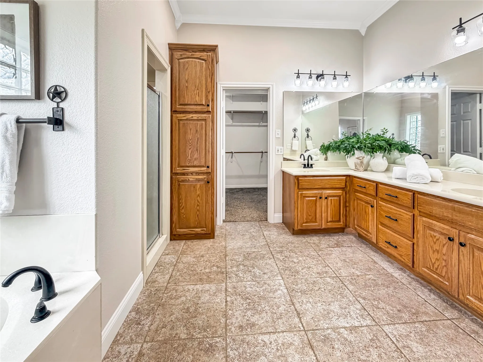 Spacious bathroom featuring a dual vanity with wood-finish cabinetry, a separate shower enclosure, a built-in soaking tub with a black-finish faucet, and tiled flooring