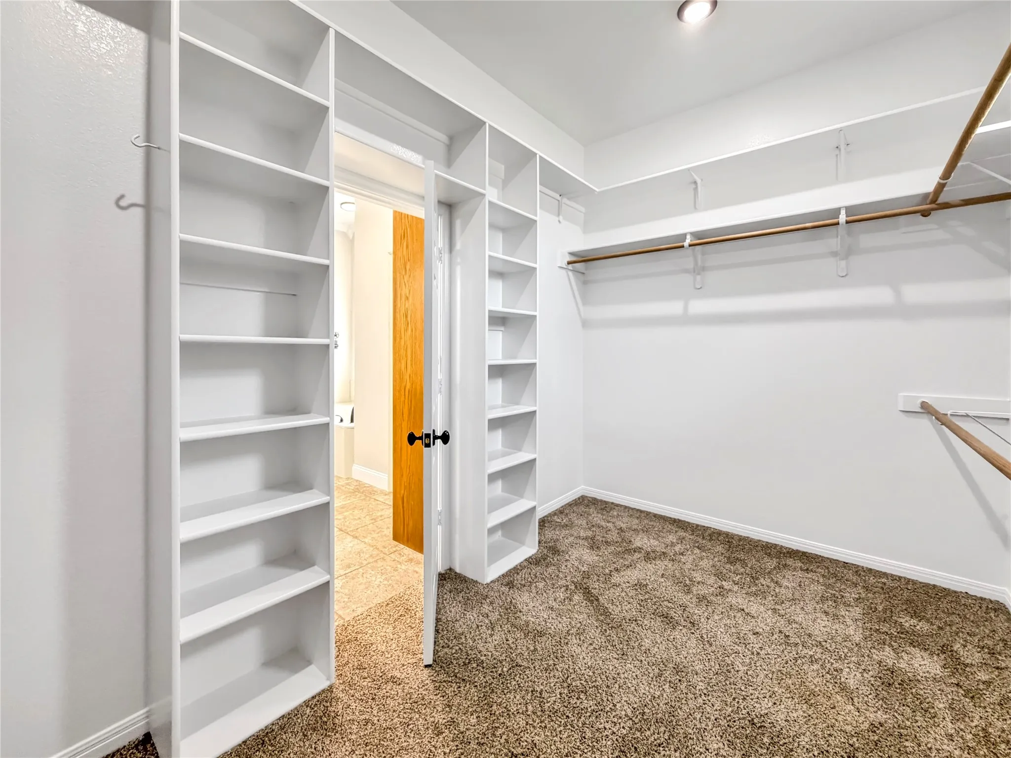 Custom closet system featuring extensive built-in shelving, two hanging rods, recessed ceiling lighting, and carpet flooring