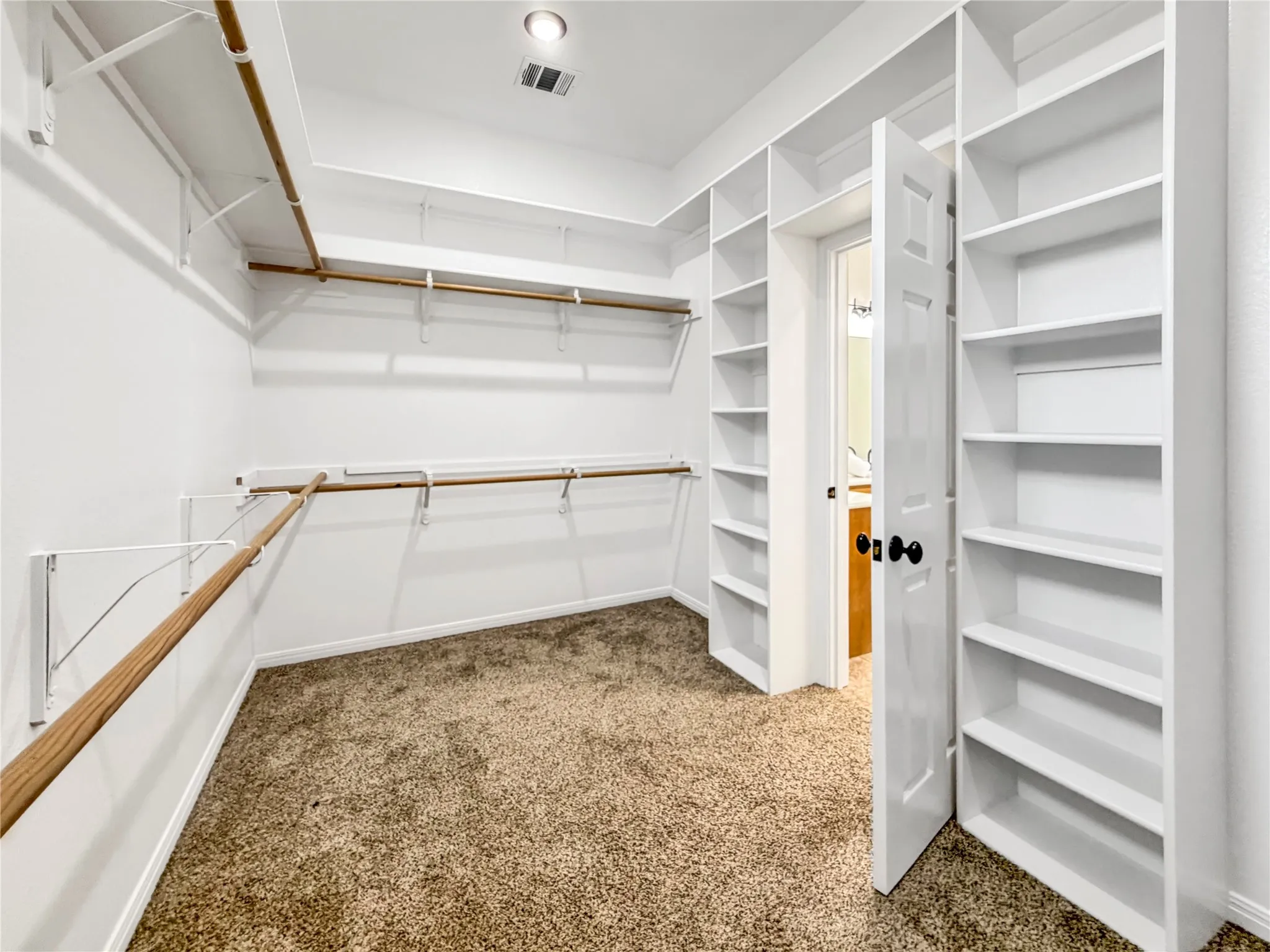 Walk-in closet featuring extensive built-in shelving, multiple hanging rods, recessed lighting, and carpet flooring