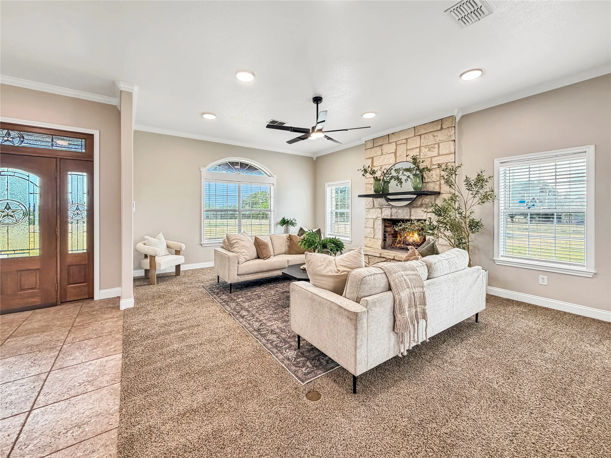 Spacious living area featuring a stone-clad fireplace with a dark wood mantel, recessed lighting, and a contemporary ceiling fan