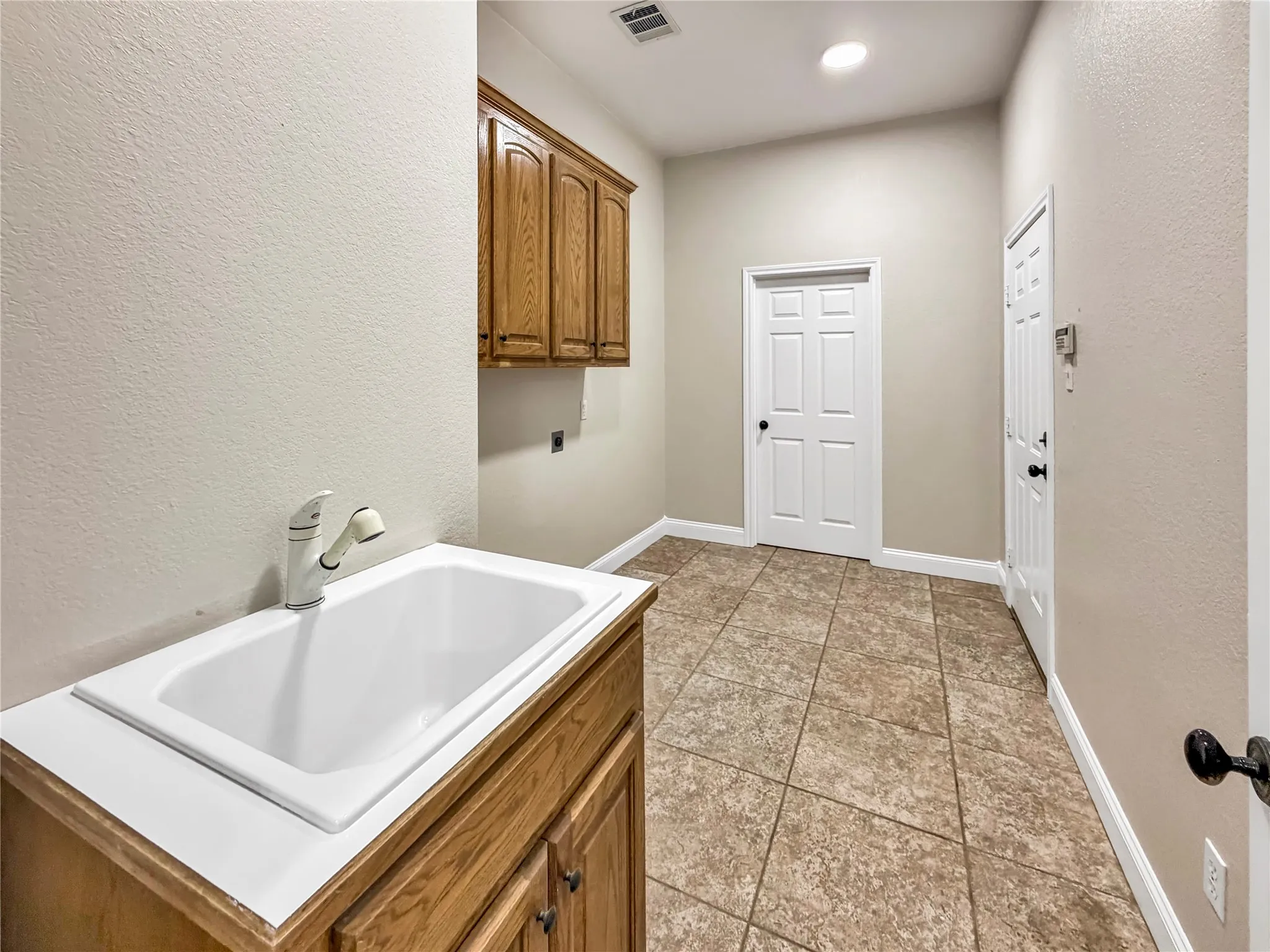 Utility room featuring a built-in wash basin with a white countertop, wood-finish cabinetry, and tiled flooring