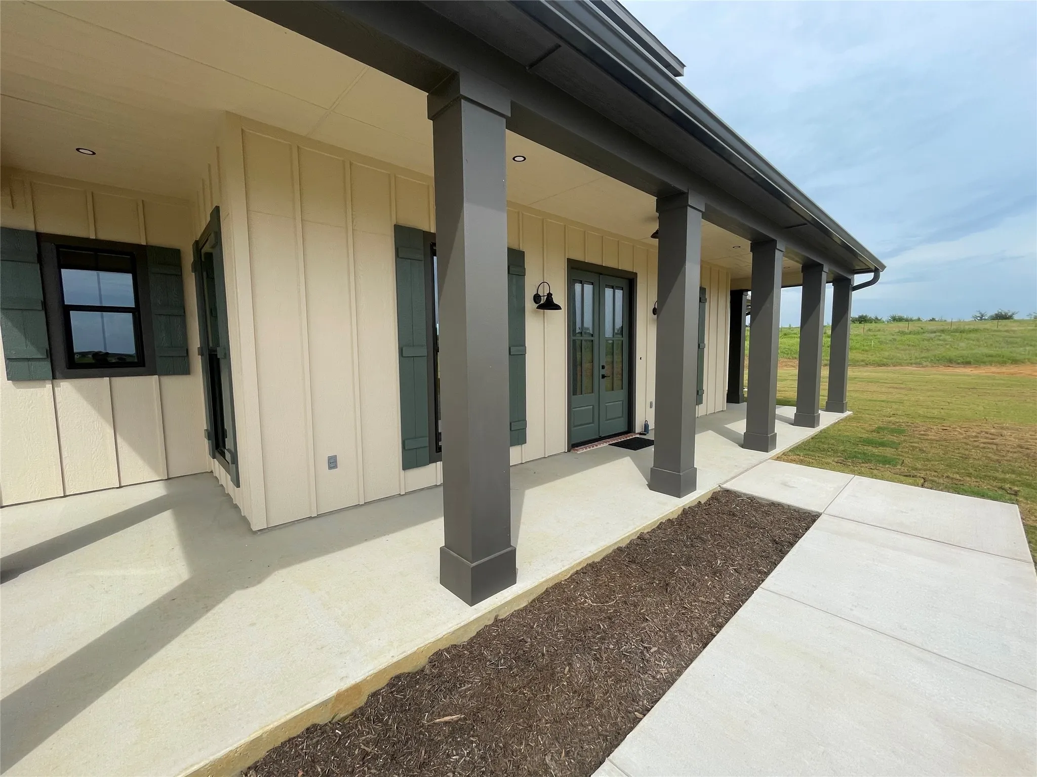 Expansive covered porch featuring a series of dark gray columns, light cream board and batten siding, and dark green shutters