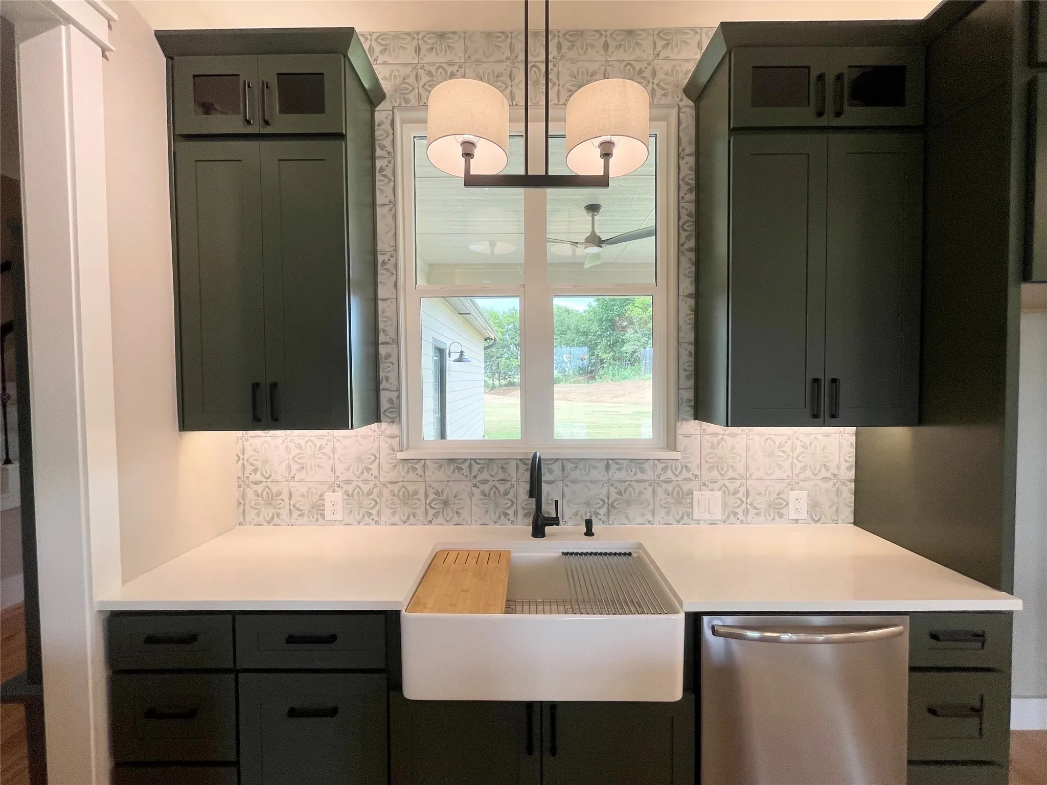 Kitchen featuring deep green cabinetry with matte black hardware, white countertops, and a patterned backsplash