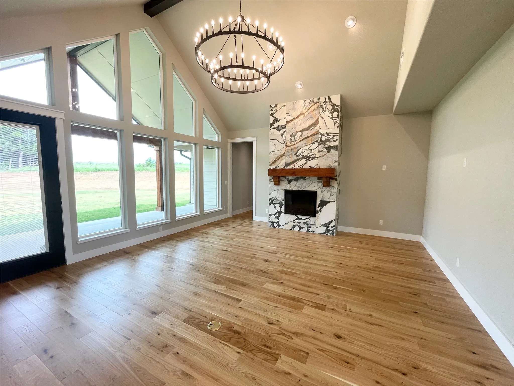 Spacious living area featuring a vaulted ceiling with exposed beam, a multi-tiered chandelier, and a floor-to-ceiling fireplace with an integrated wood mantel and stone surround