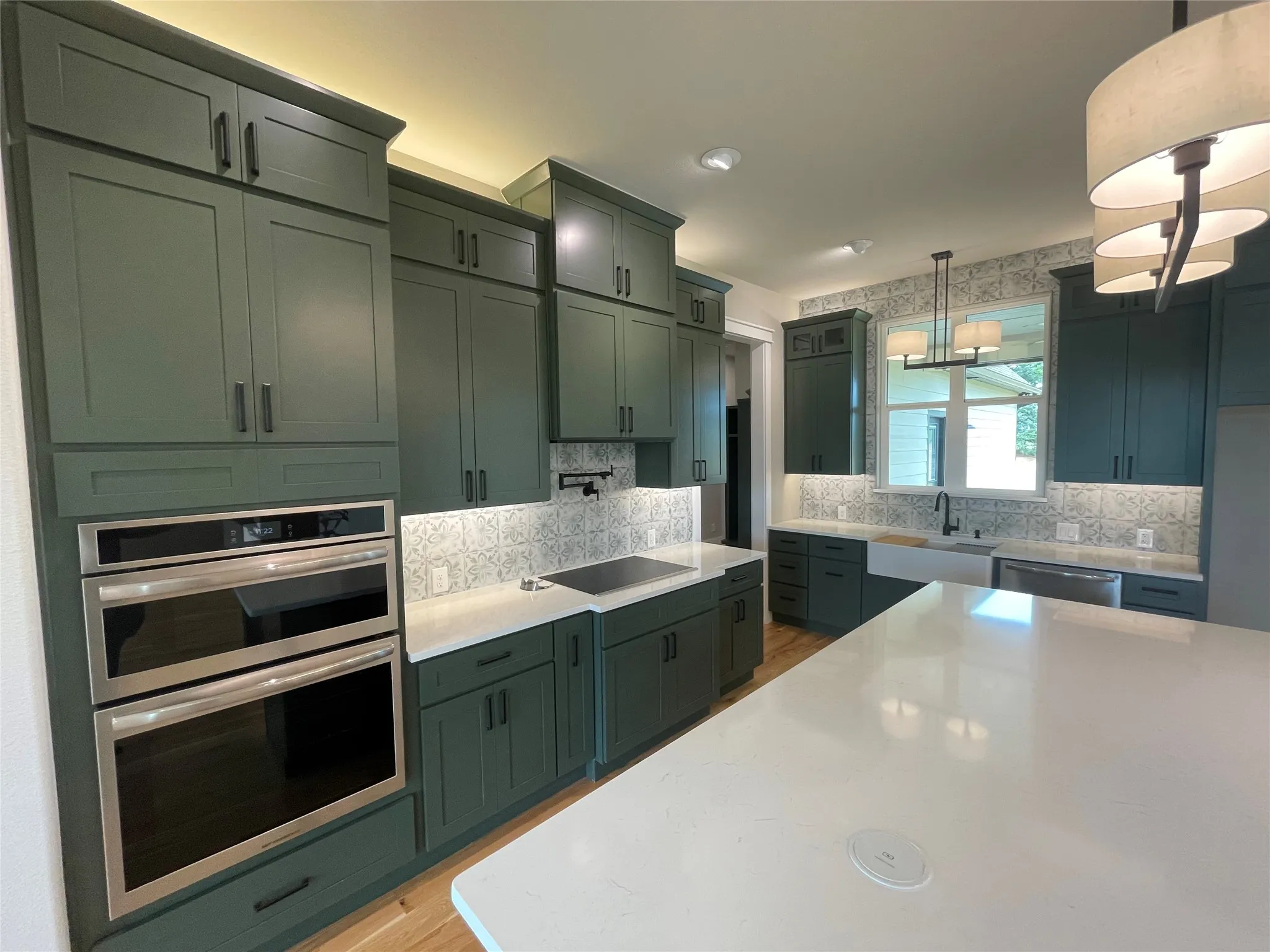 Kitchen featuring dark green cabinetry, white countertops, built-in double ovens, a white farmhouse sink, and a patterned tile backsplash
