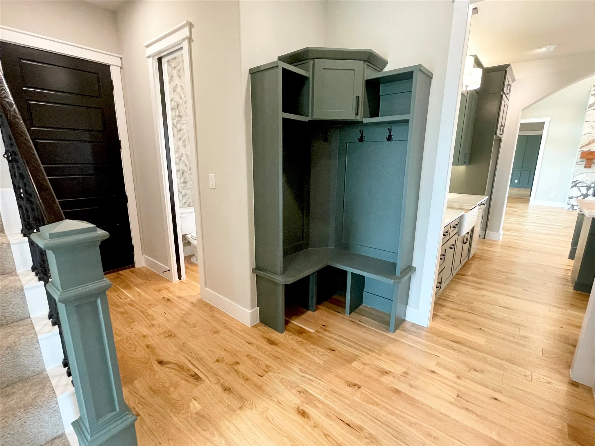 Entryway featuring light wood-finish flooring, a built-in storage bench with cabinetry, a dark paneled door, a staircase with a dark metal railing, and a coordinating newel post
