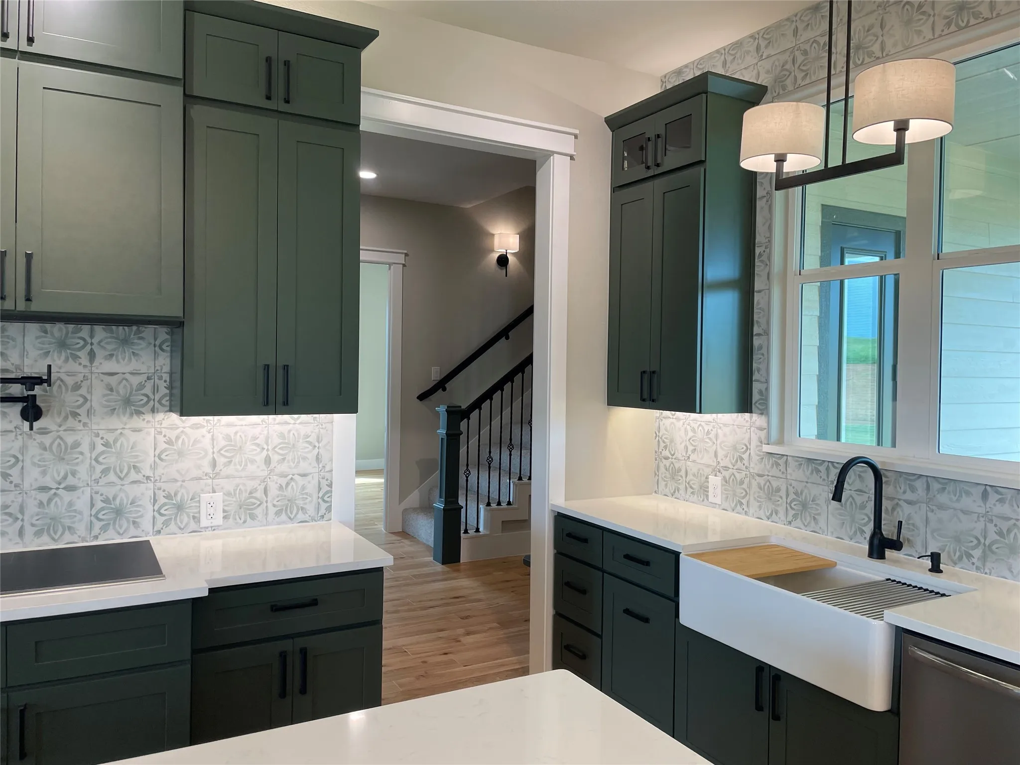Kitchen featuring forest green cabinetry with dark hardware, a white farmhouse-style sink, and a decorative tile backsplash