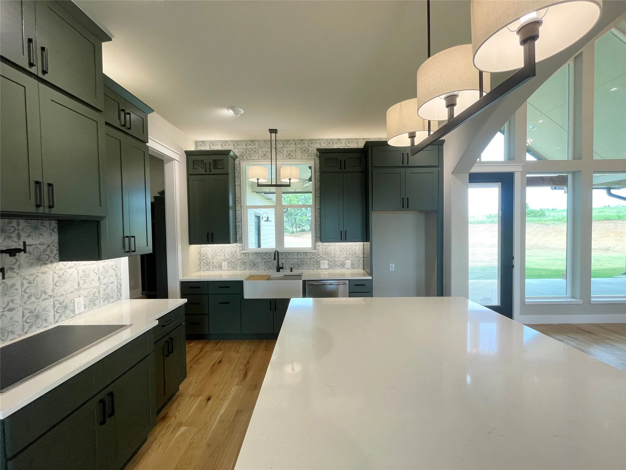 Gourmet kitchen featuring dark green cabinetry, a large white countertop island, wood-finish flooring, a farmhouse sink, and a patterned tile backsplash