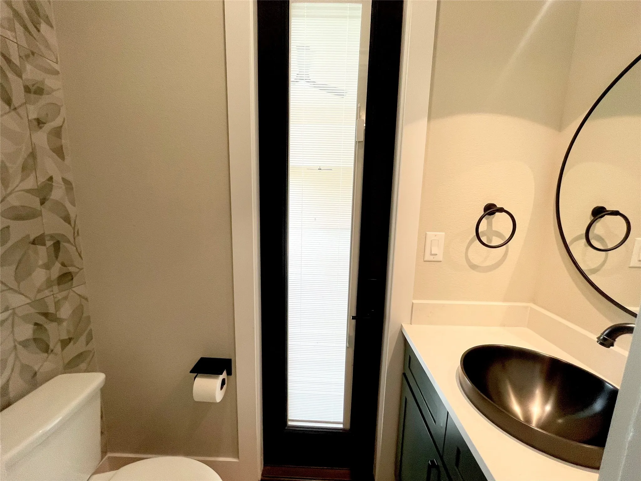 Modern bathroom vanity featuring a dark vessel sink, light countertop, and a circular wall mirror with a dark frame