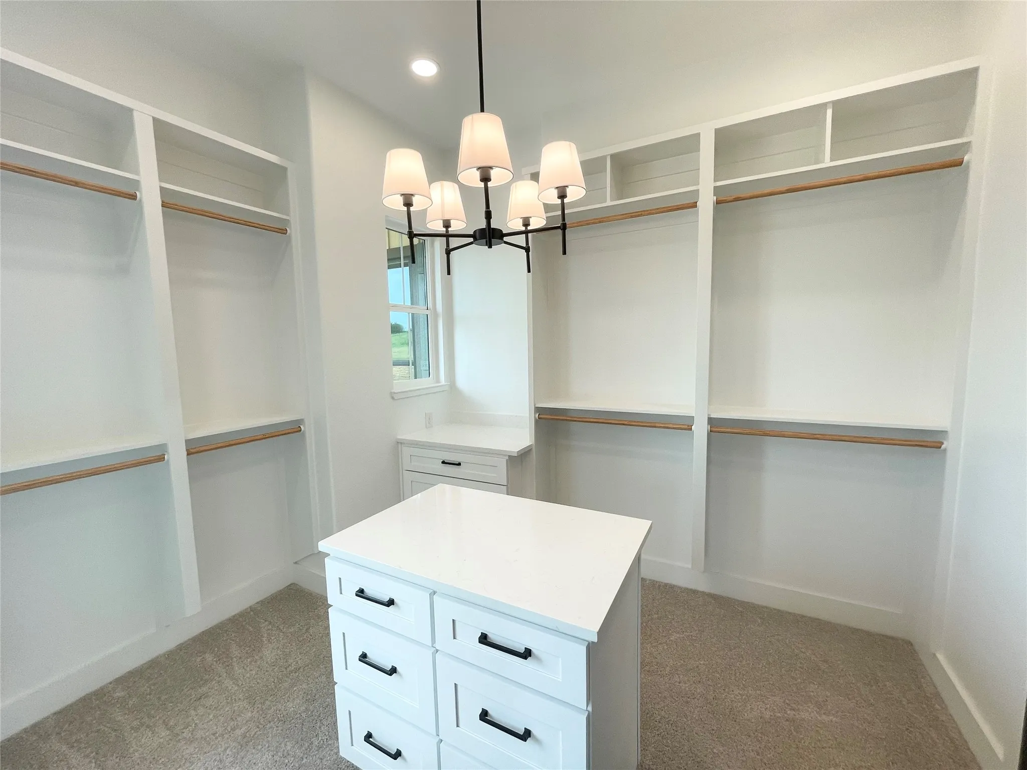 Spacious custom closet featuring a central island with six drawers, extensive built-in shelving, multiple hanging rods, and a window providing natural light
