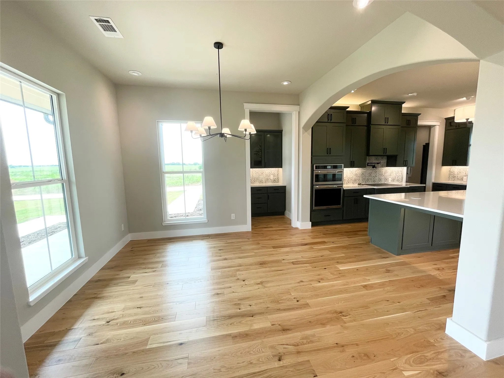 Spacious interior featuring light wood-finish flooring, multiple windows, and a modern chandelier