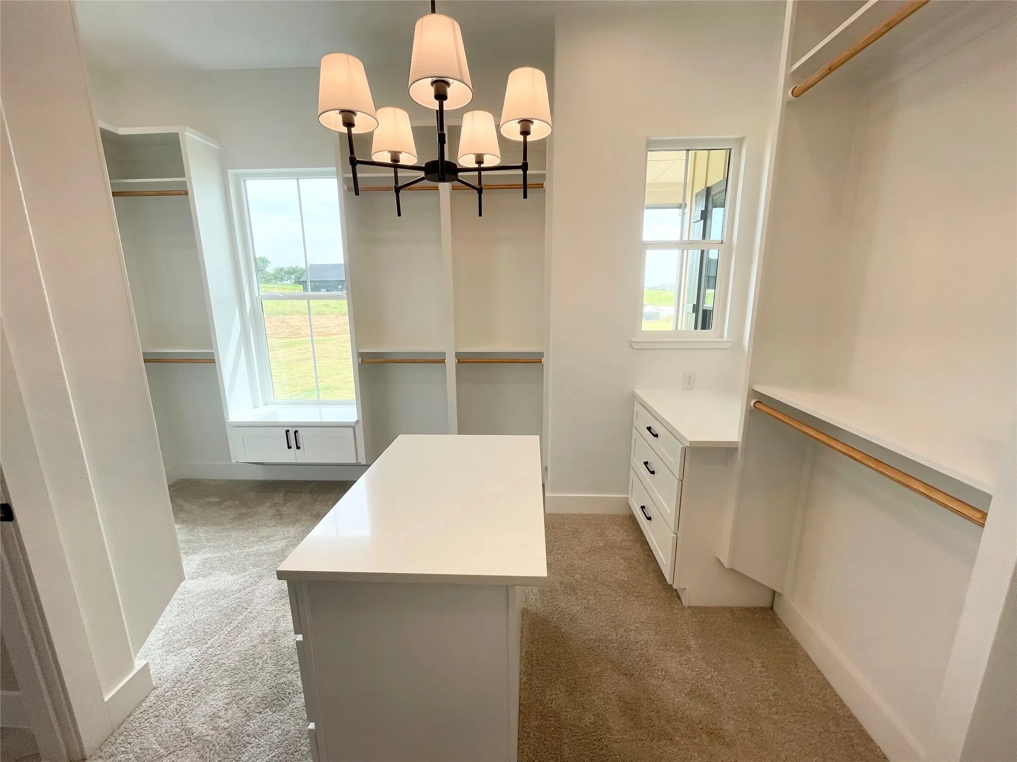 Spacious walk-in closet featuring a central island, built-in shelving, hanging rods, an integrated window seat with storage, and a multi-light chandelier