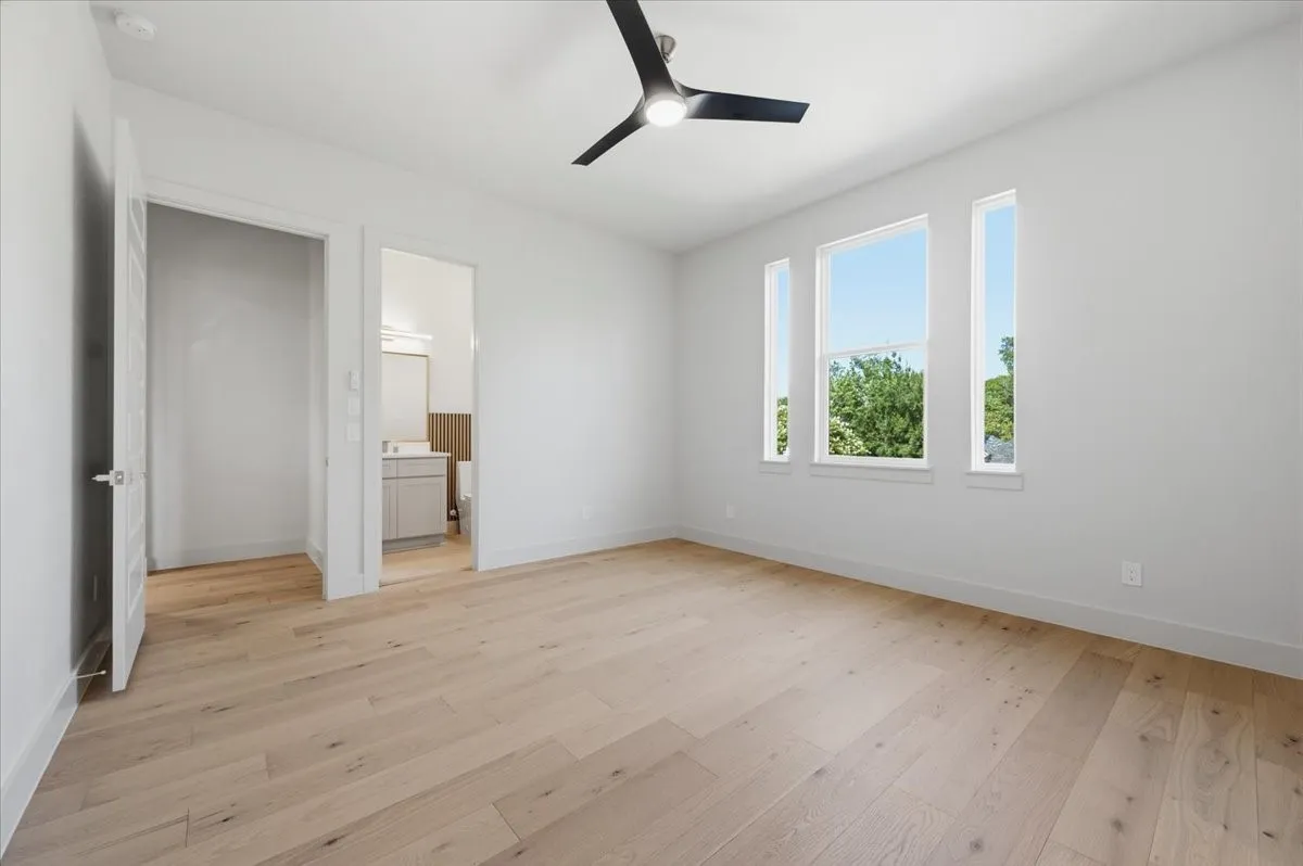 Spacious room featuring wood-finish flooring, multiple windows, a modern ceiling fan, and crisp white walls