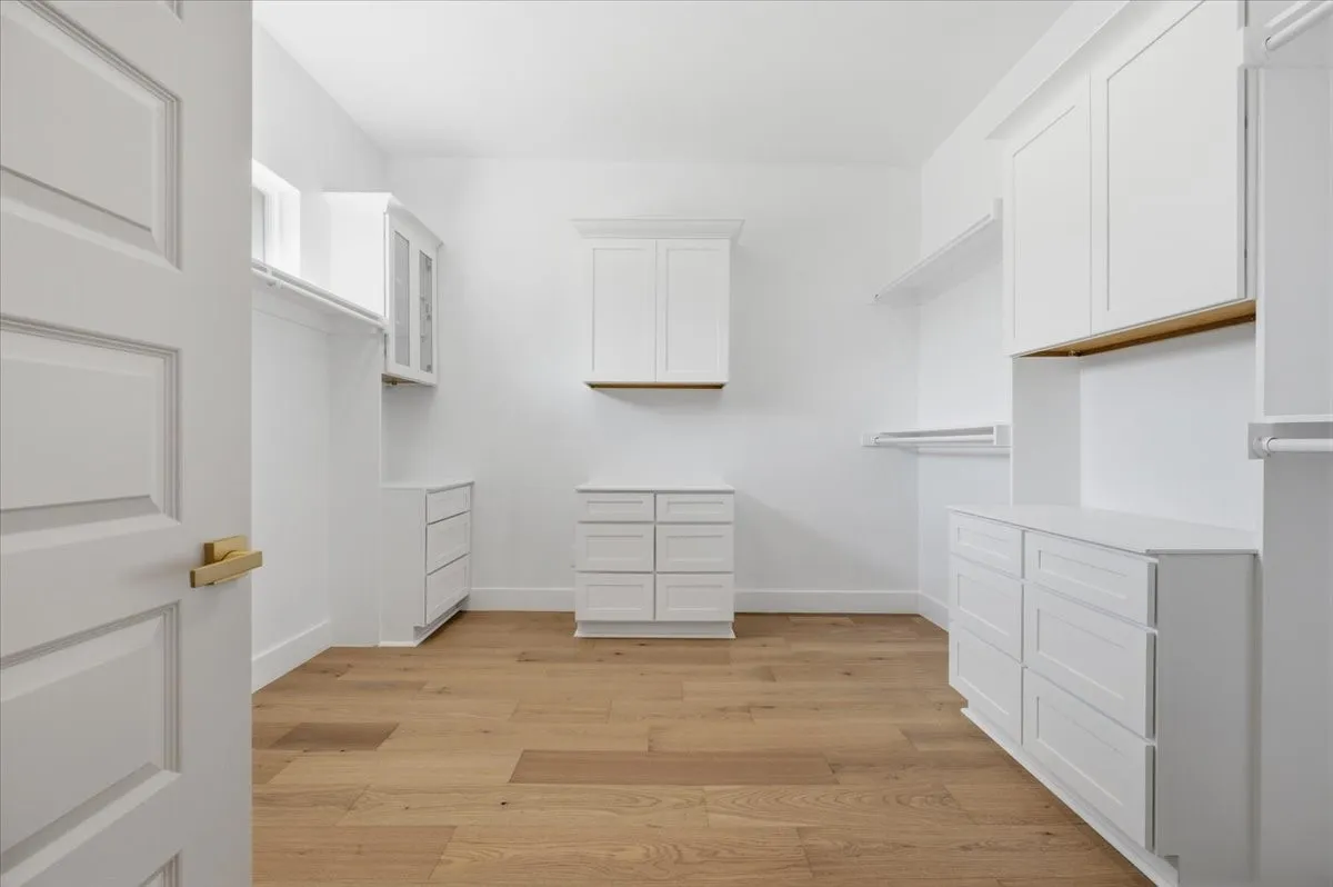 Spacious custom closet featuring wood-finish flooring, white built-in cabinetry, integrated drawers, and ample hanging rods