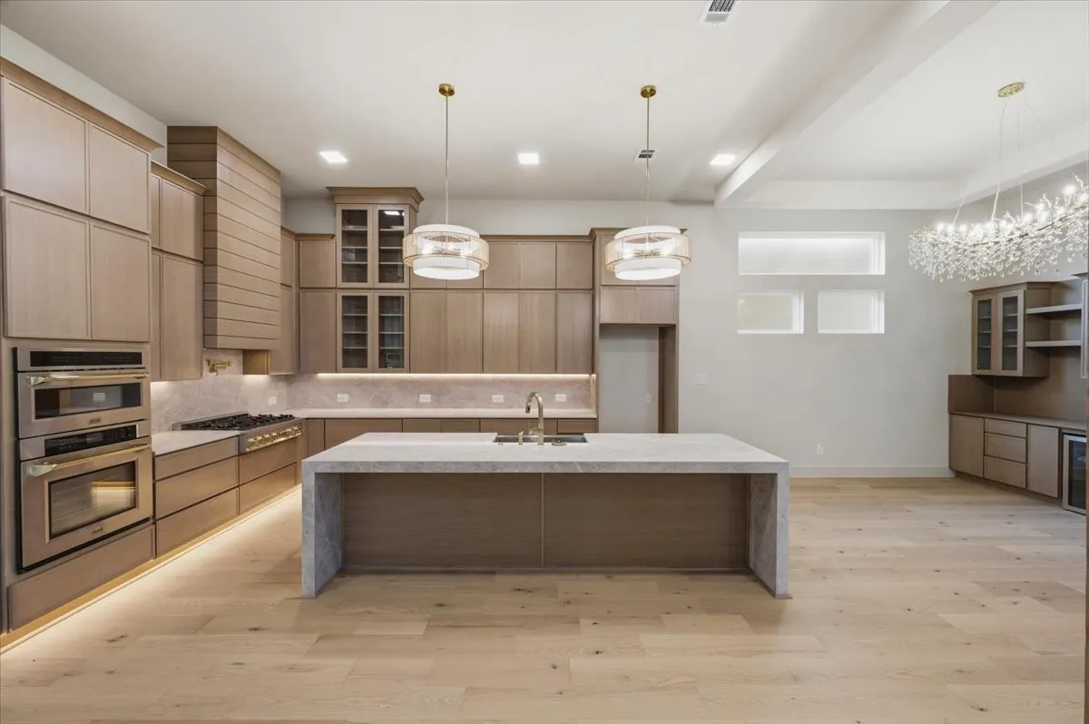 Gourmet kitchen with light wood-finish cabinetry, a waterfall island, stainless steel appliances, and a gas range