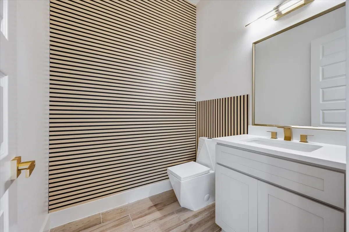 Modern powder room featuring a white vanity with integrated sink, brass-finish fixtures, and a statement slatted wood-panel accent wall