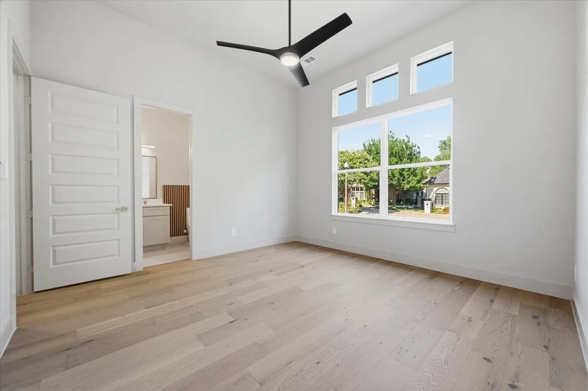 Spacious room with high ceilings, light wood-finish flooring, and a contemporary ceiling fan