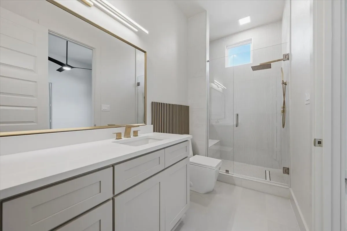 Contemporary bathroom featuring a spacious vanity with white countertops, integrated sink, and gold-finish fixtures