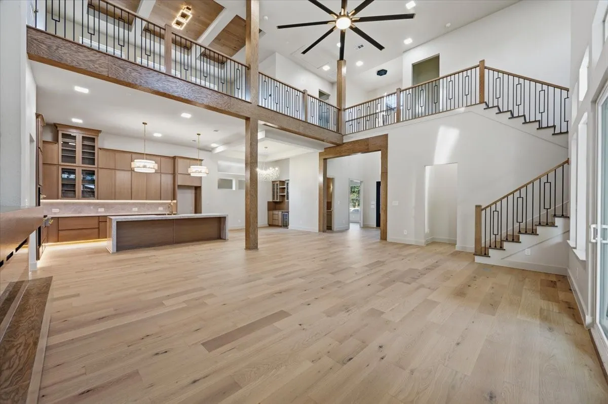 Open-concept living space featuring wood-finish flooring, a two-story ceiling, and a prominent staircase with decorative metal balusters
