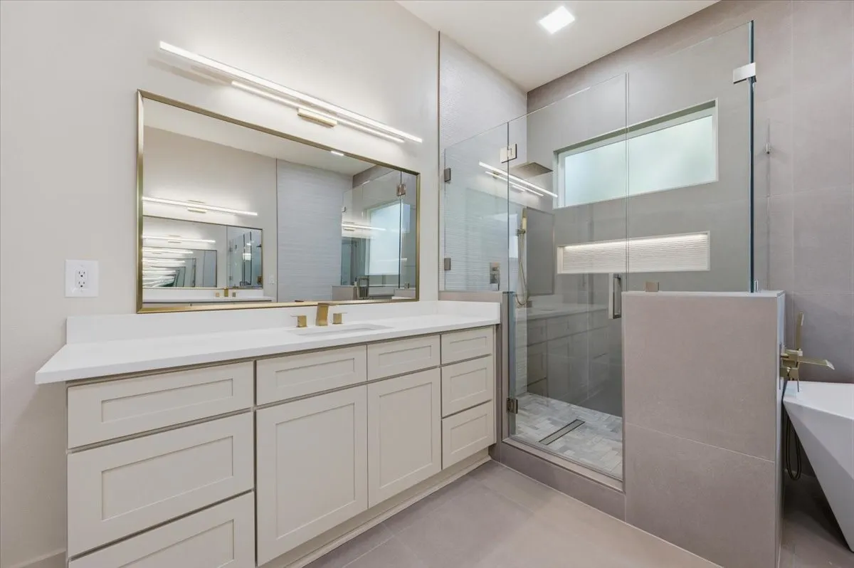 Modern bathroom featuring a frameless glass shower enclosure, a vanity with a white countertop, and brushed gold fixtures