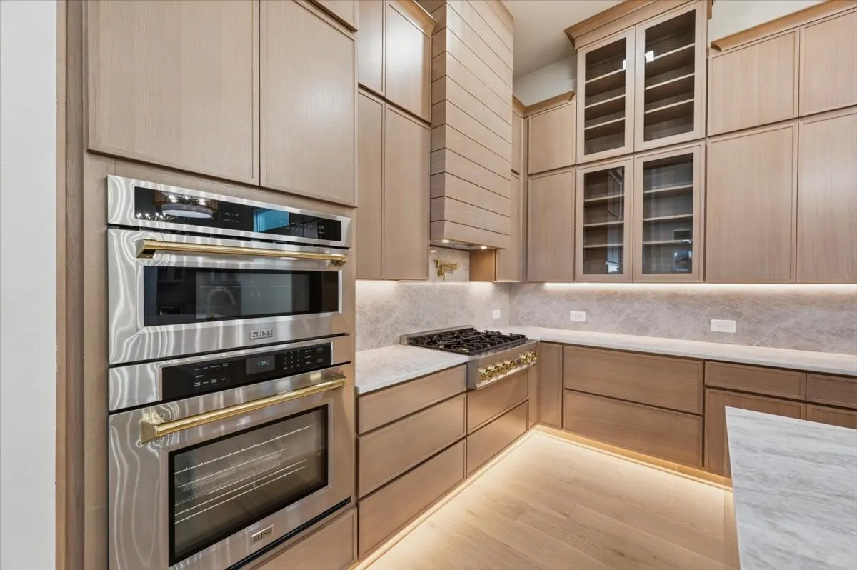 Modern kitchen featuring integrated stainless steel appliances, custom wood cabinetry, marble countertops, and under-cabinet lighting