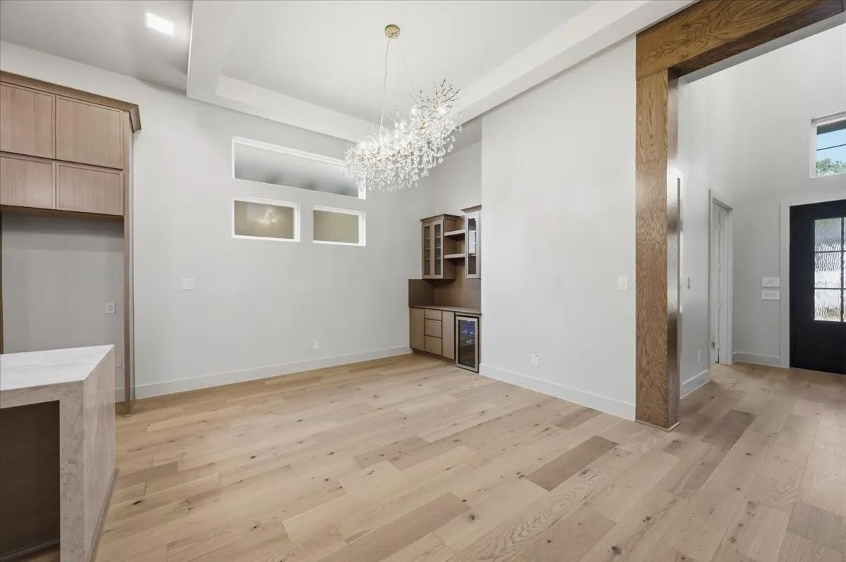 Spacious interior featuring light wood-finish flooring, a built-in wet bar with beverage refrigerator, and a sparkling crystal chandelier