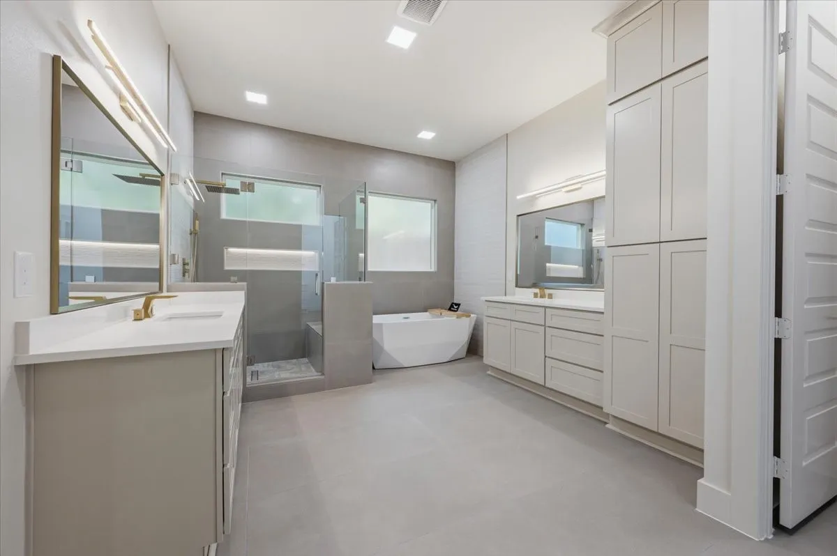 Spacious bathroom featuring a freestanding tub, expansive walk-in shower with bench, dual vanity areas with ample cabinetry, light-toned flooring, and integrated lighting
