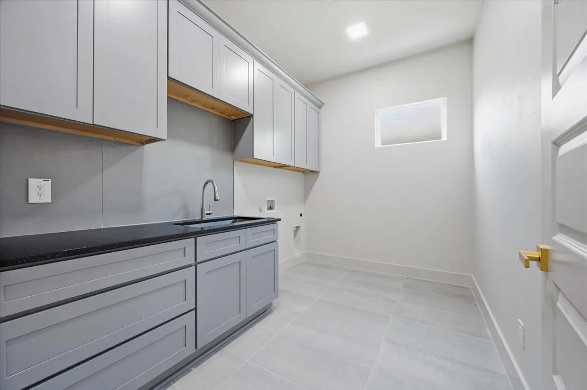Utility room featuring extensive grey shaker cabinetry, a dark countertop, a stainless steel sink with a gooseneck faucet, and tiled flooring
