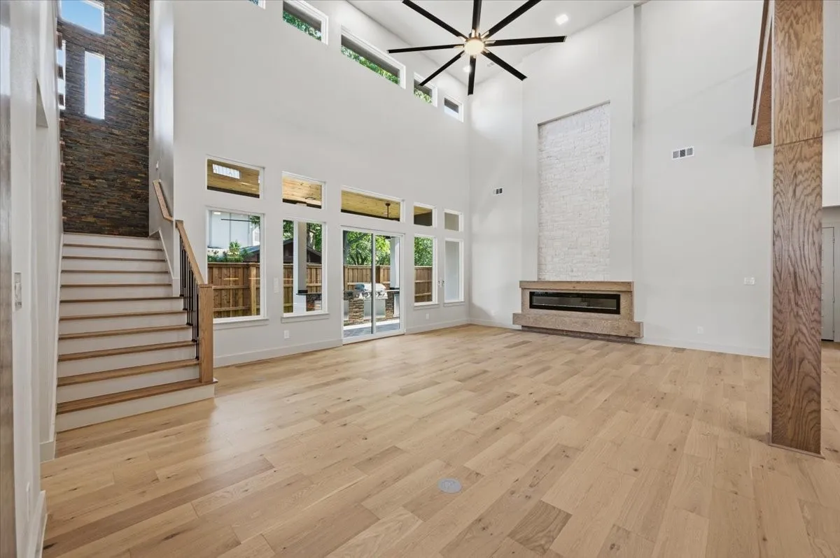 Spacious living area featuring high ceilings, light wood-finish flooring, and a linear fireplace with a textured surround