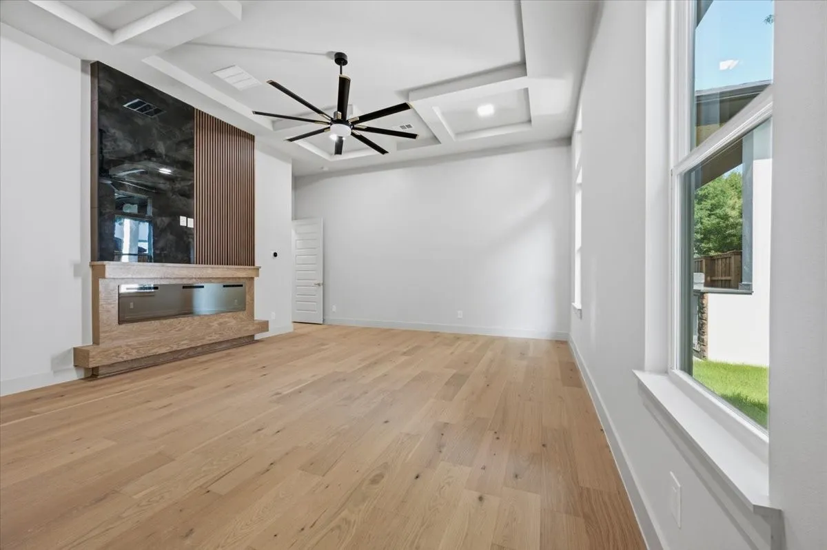 Spacious room featuring light wood-finish flooring, a contemporary fireplace with a dark paneled surround, and a modern ceiling fan