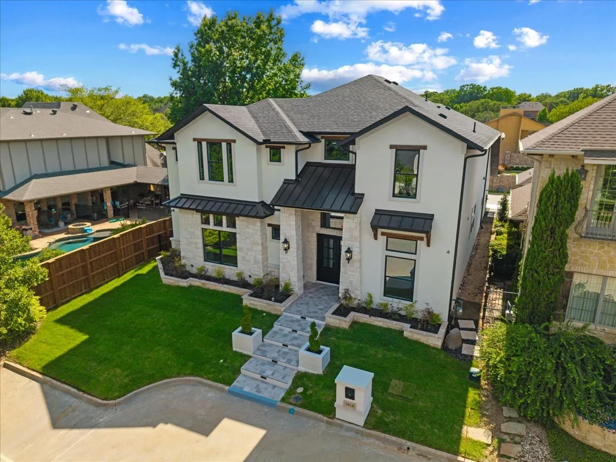 Contemporary residence featuring a white stucco and stone facade, dark roofing, and black window frames