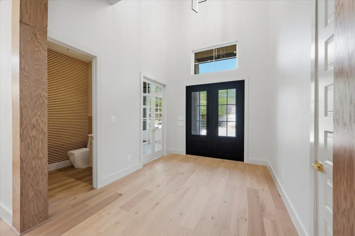 Double-height entry foyer featuring light wood-finish flooring, white walls, and a transom window above double black entry doors