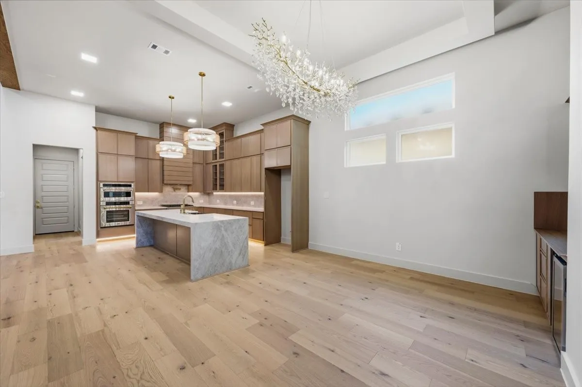 Contemporary kitchen featuring wood-finish cabinetry, a waterfall island, dual wall ovens, and wood-finish flooring