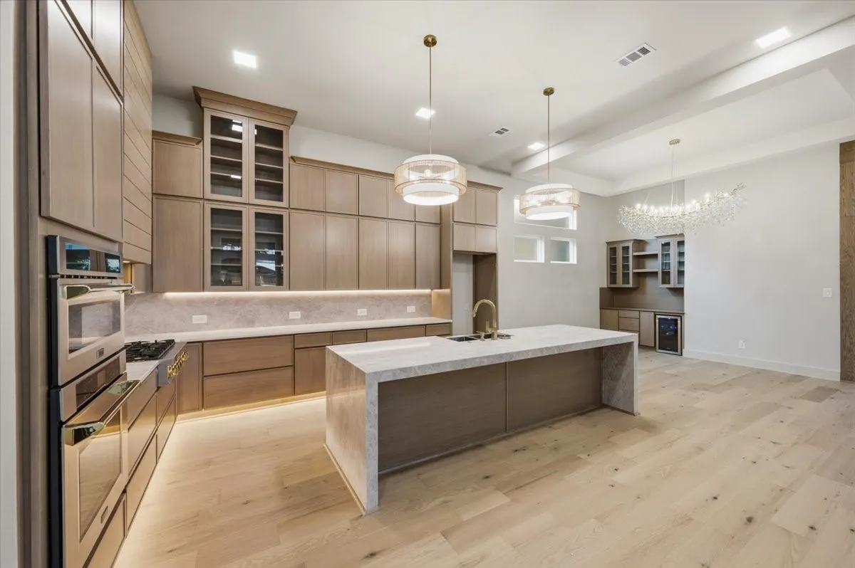 Expansive kitchen featuring a large waterfall island with a sink, light wood-finish flooring, and integrated stainless steel appliances