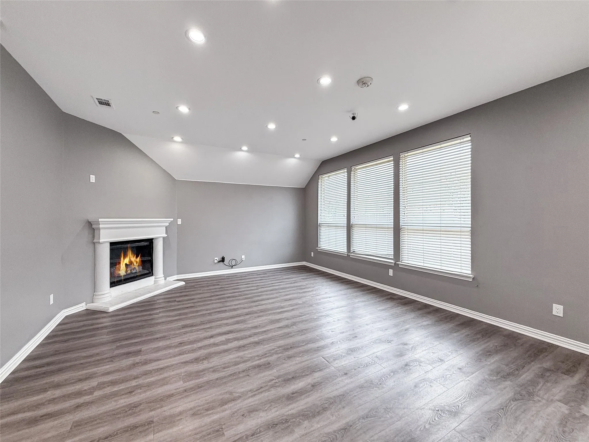 Spacious living area featuring high vaulted ceilings, recessed lighting, a built-in fireplace with a white mantel, and wide wood-finish flooring
