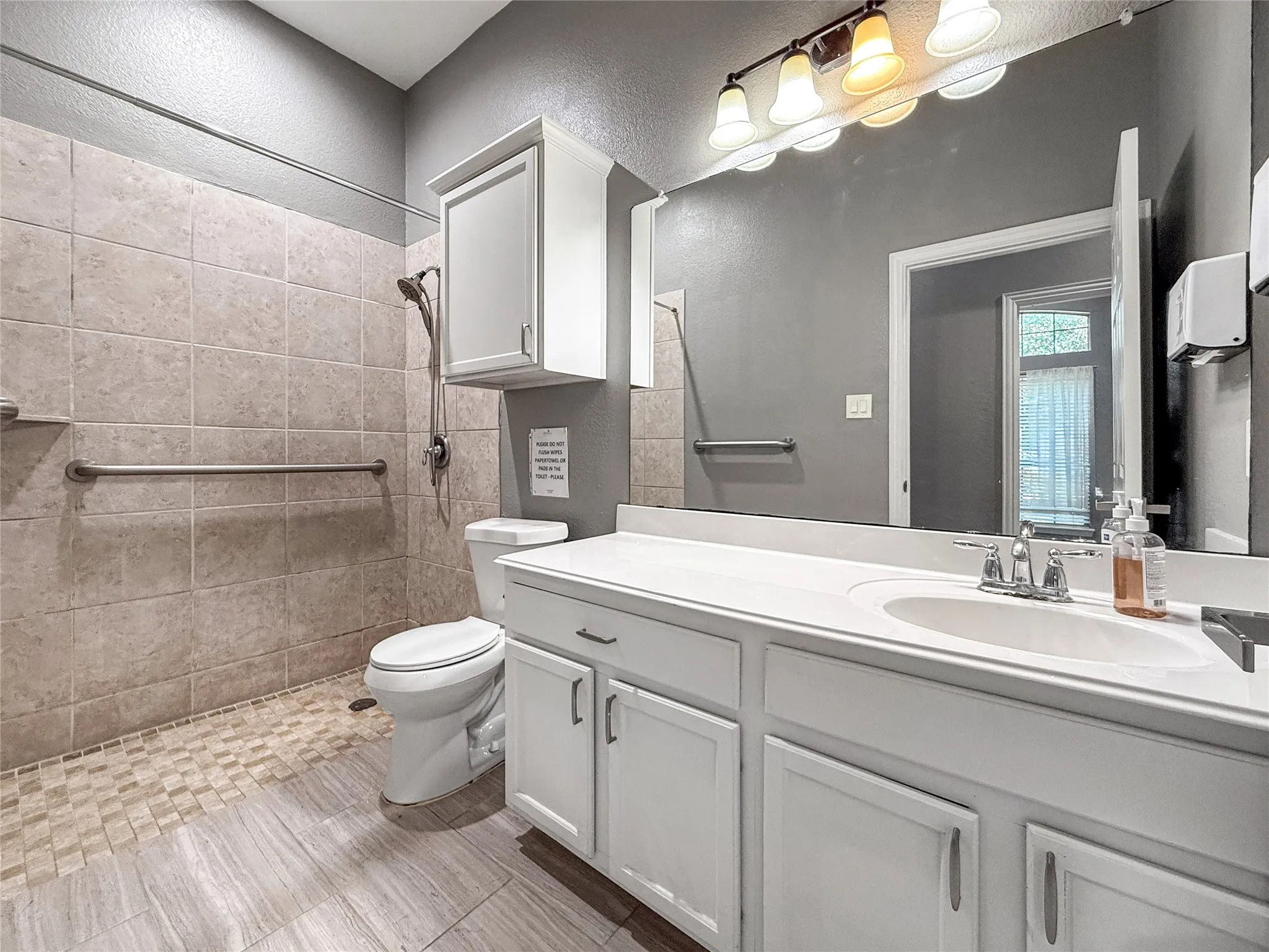 Bathroom featuring a walk-in shower with tile surround, a single vanity with storage, a large wall-mounted mirror, and wood-finish flooring