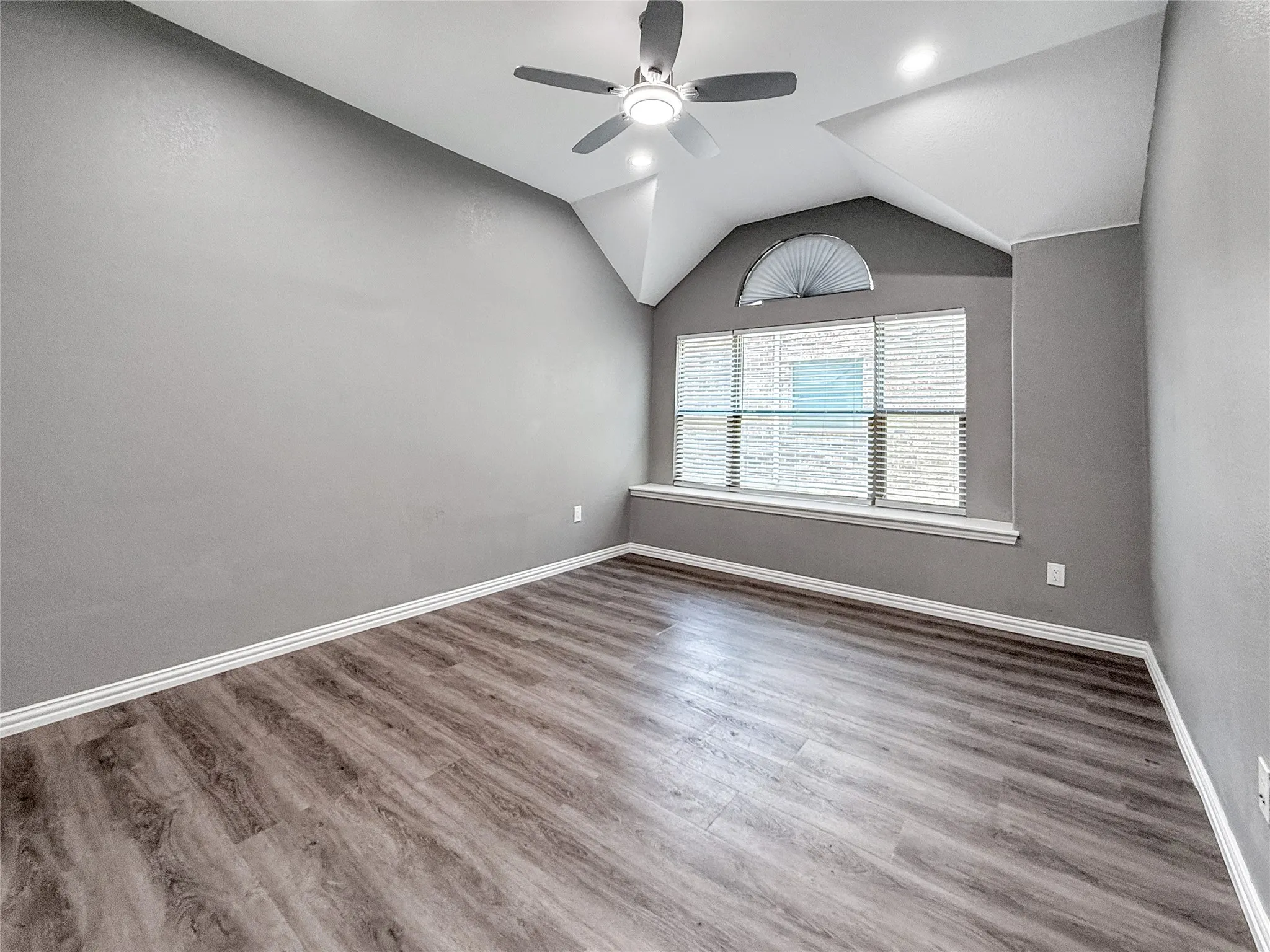 Spacious room featuring wood-finish flooring, vaulted ceilings, and a ceiling fan