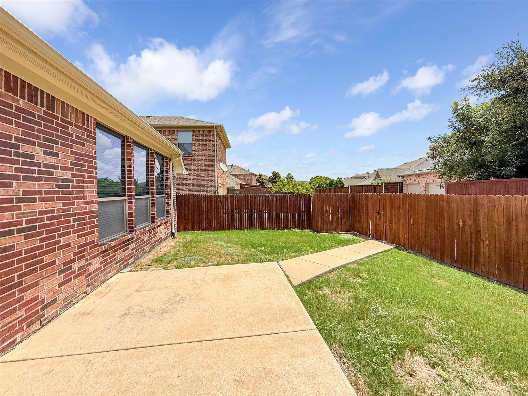 Private backyard featuring a concrete patio, perimeter wood fencing, and a manicured lawn