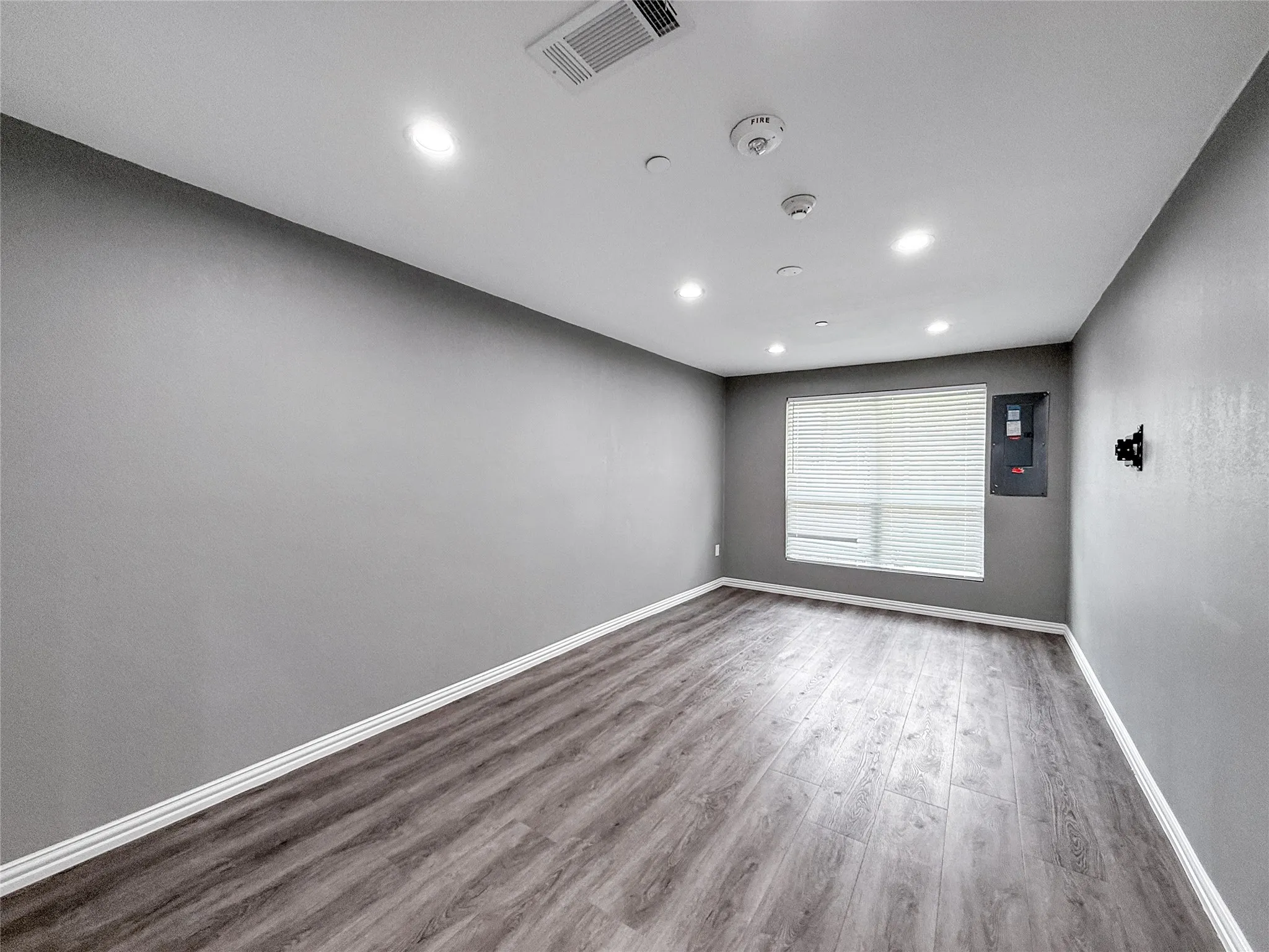 Spacious room featuring wood-finish flooring, recessed lighting, and a window with blinds
