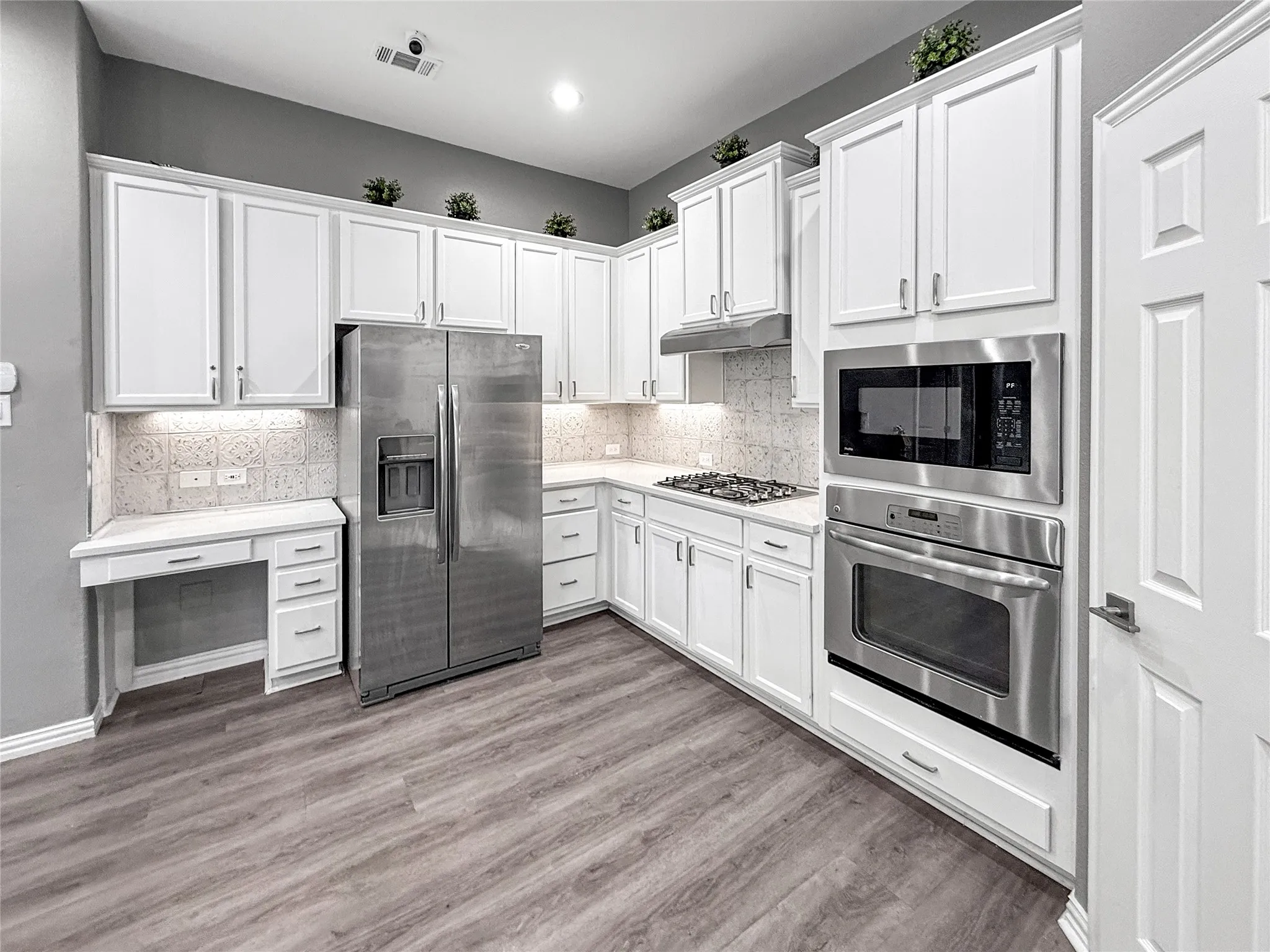 Modern kitchen featuring white cabinetry, stainless steel appliances, wood-finish flooring, a built-in oven and microwave, and a gas cooktop