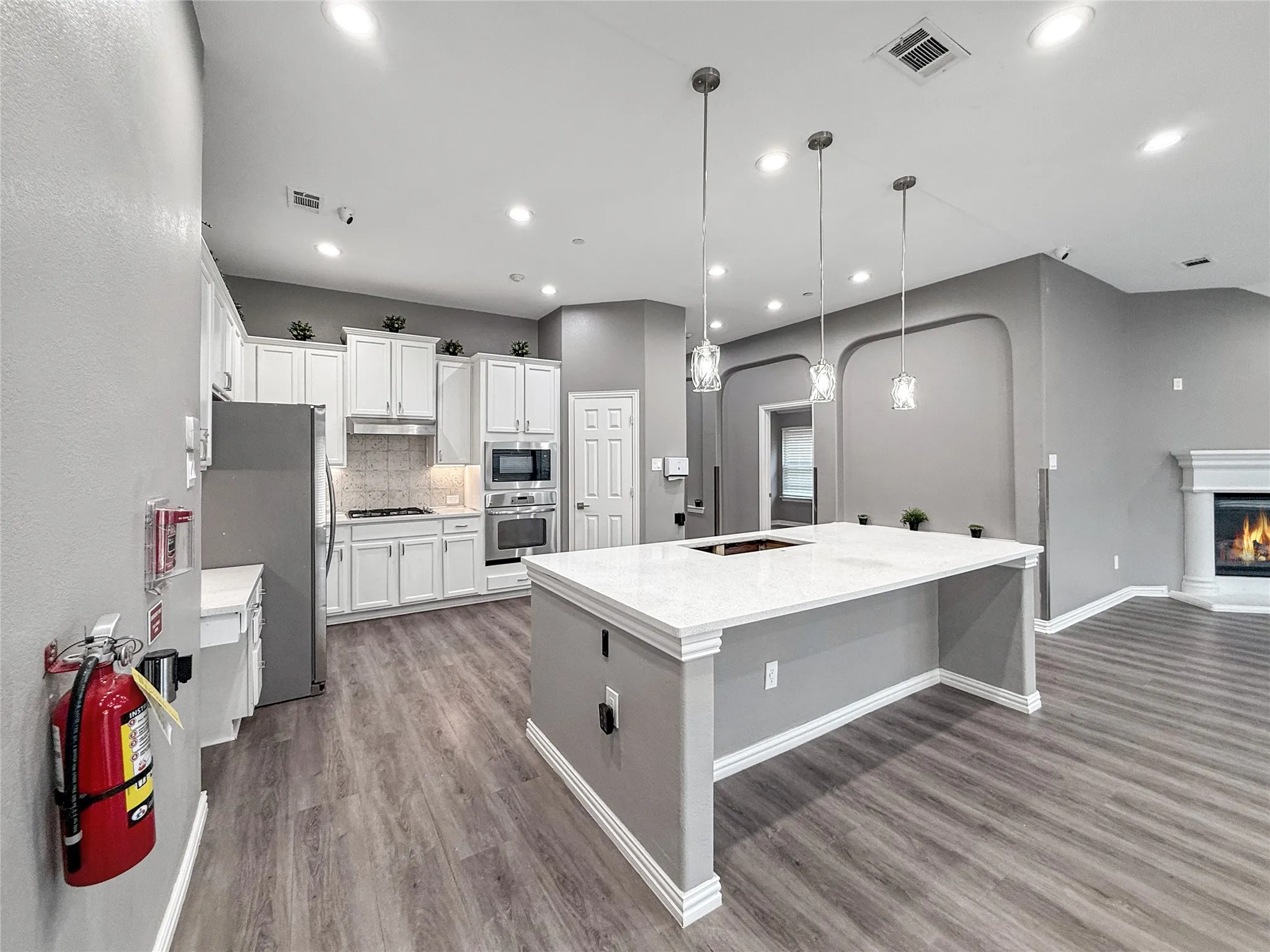 Spacious kitchen featuring an expansive island with a white countertop, white cabinetry, stainless steel appliances, and wood-finish flooring