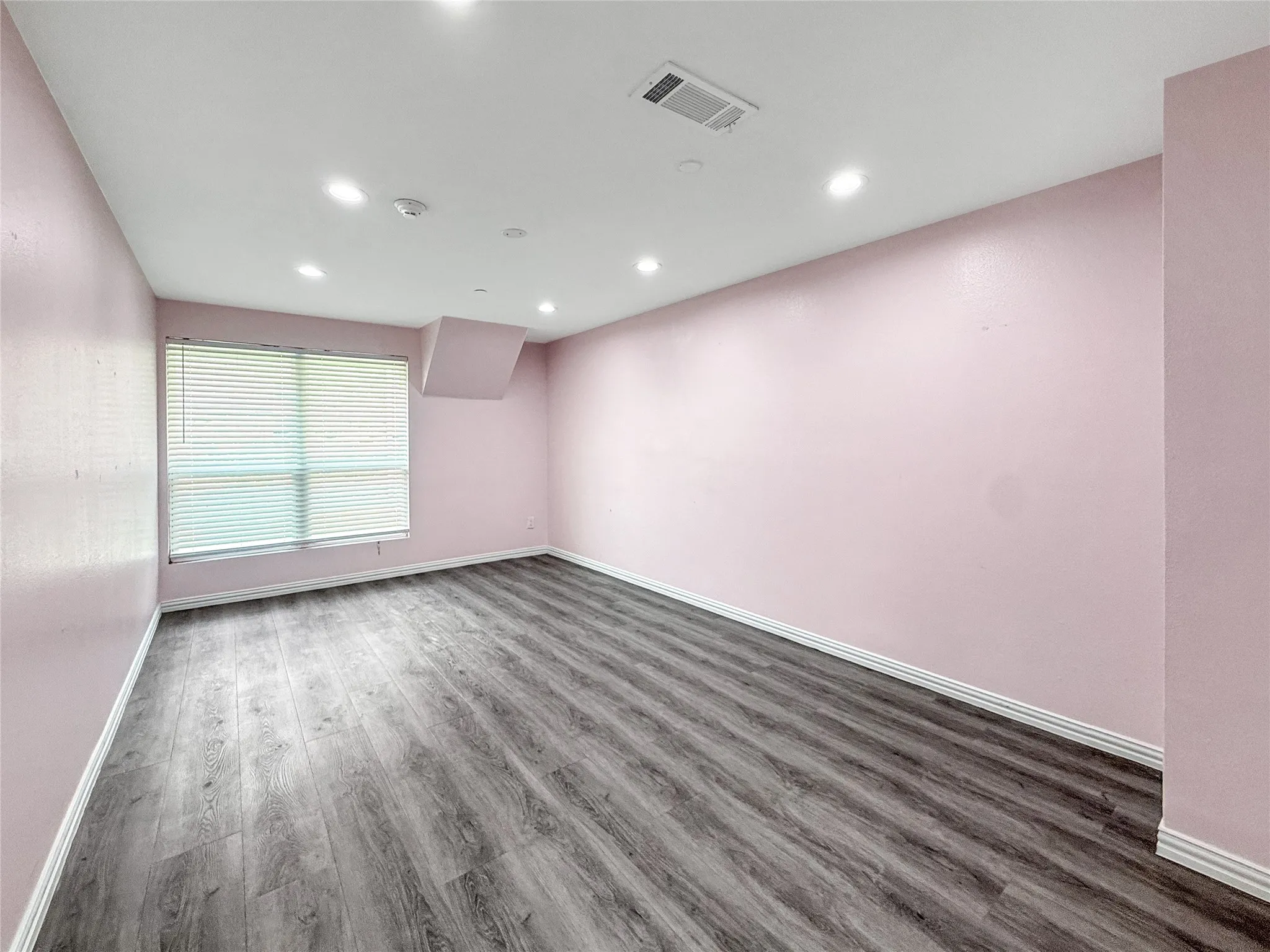 Spacious room featuring wood-finish flooring, a window with horizontal blinds, recessed ceiling lighting, and a white baseboard trim