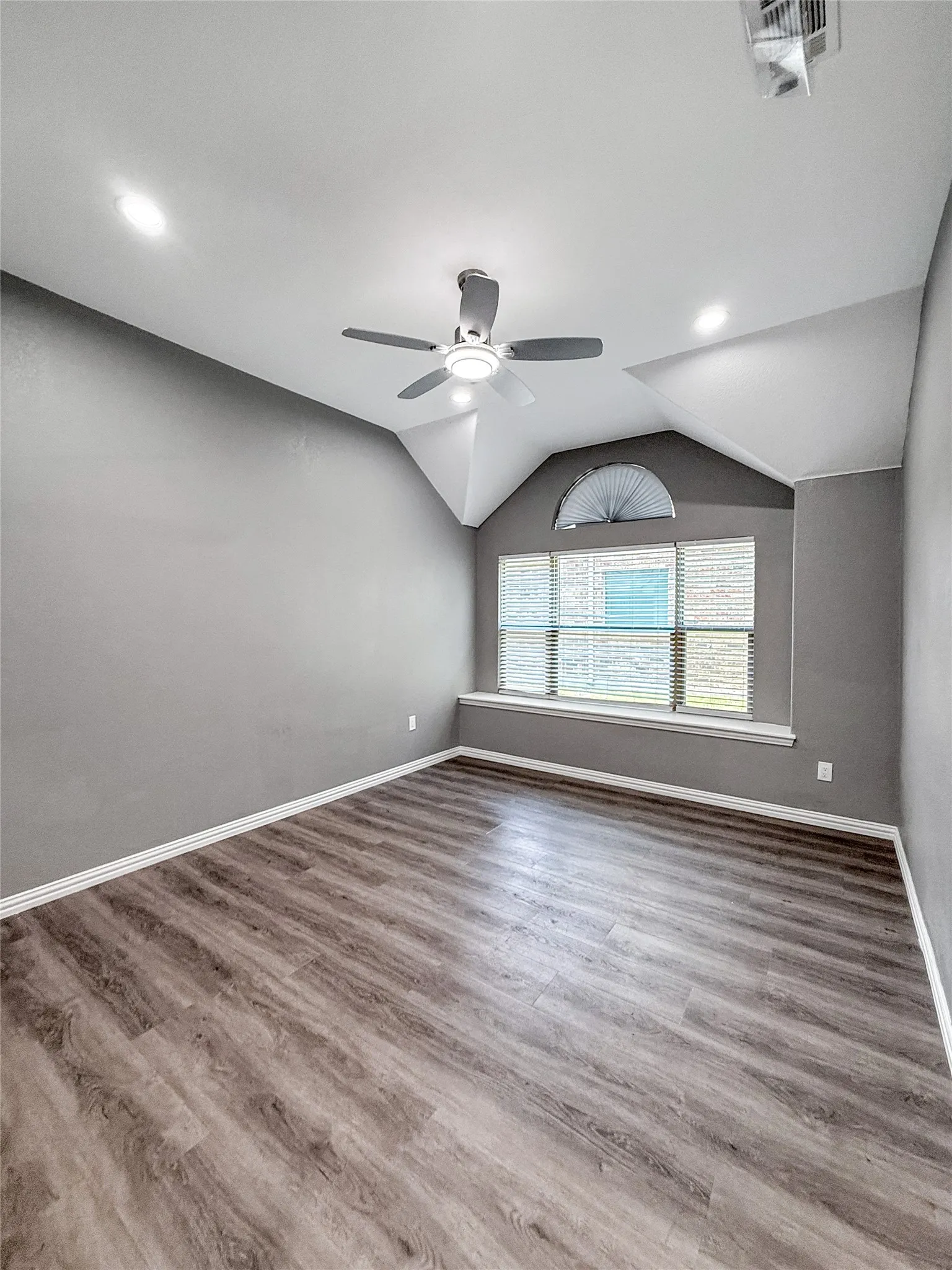 Spacious room featuring wood-finish flooring, vaulted ceilings, and a ceiling fan with integrated lighting