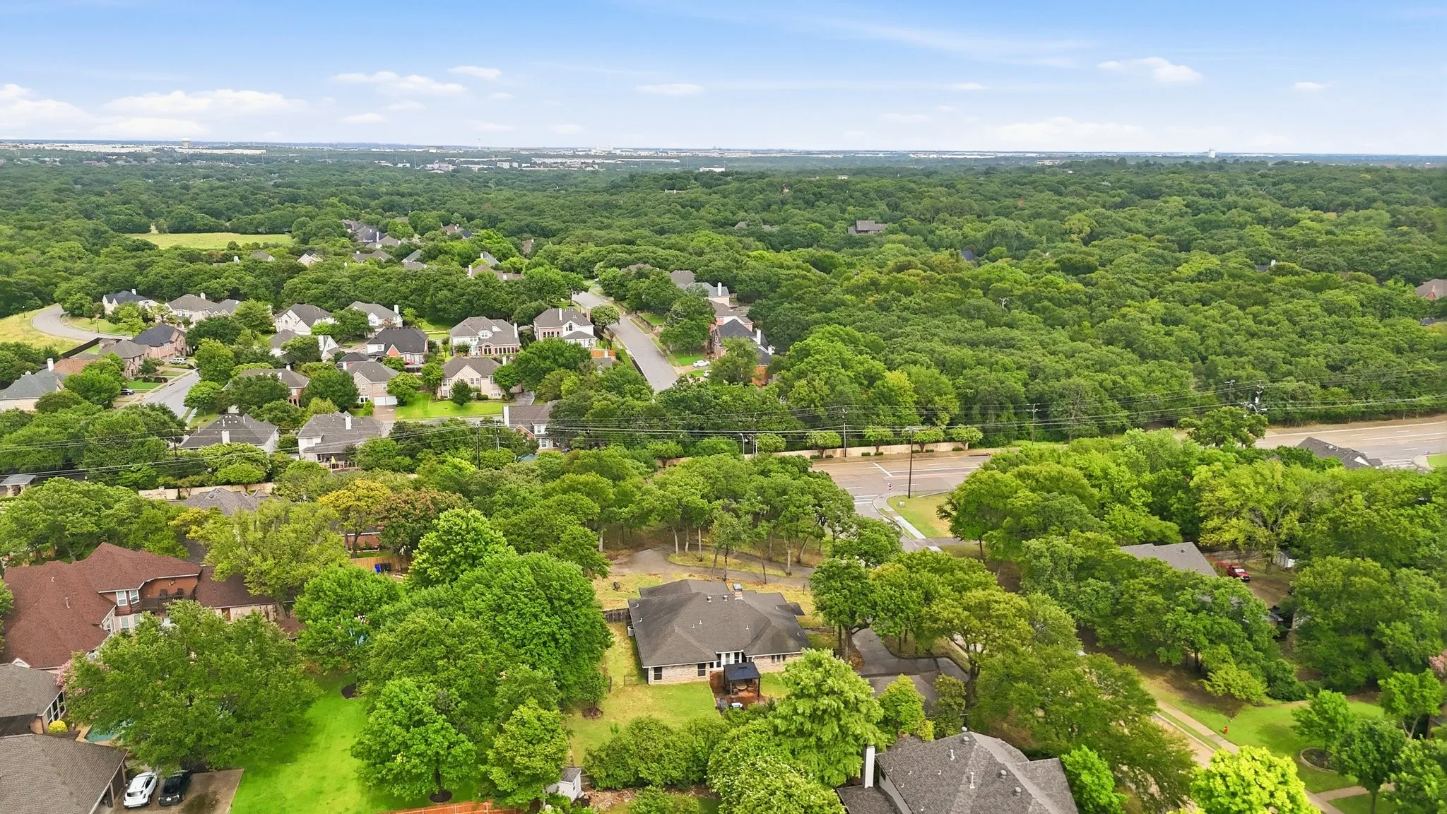 Expansive residential area featuring numerous single-family homes with gray shingle roofs, surrounded by abundant mature tree coverage