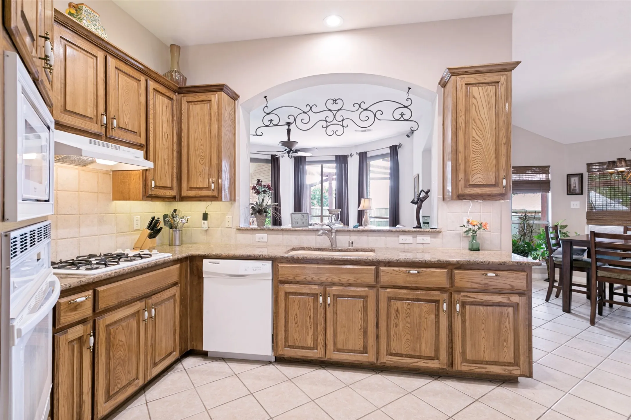 Kitchen featuring wood cabinetry with white hardware, a white built-in microwave, and a white dishwasher