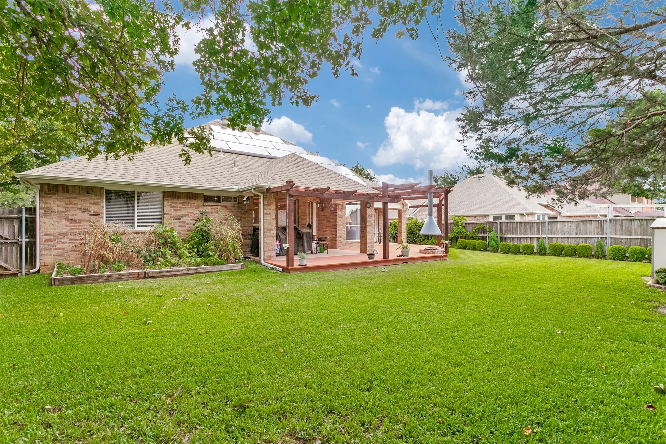 Expansive backyard featuring a lush lawn, brick exterior, wood pergola-covered patio, and solar panels on the roof